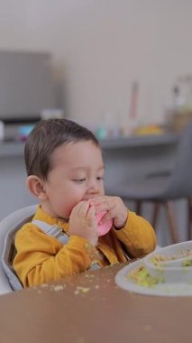 Çocuk evde masada otururken bir bardak ısırıyor. Kirli çocuk yemek yerken.