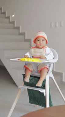 Bebek, evinin oturma odasında, sandalyesinde otururken jest yapıyor.
