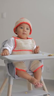 Bir bebek yemek yerken, sandalyesinde otururken masaya vurur.