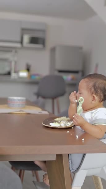 婴儿坐在桌旁 用手吃饭 拿着勺子 — 图库视频影像