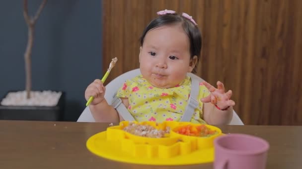 小さな女の子は 自宅でテーブルに座って食べながら手で食べ物を掴んでいました サプリメント給餌 — ストック動画