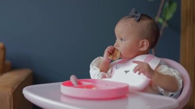 Sandalyesinde otururken elleriyle yemek yiyen bir bebeğin yüzünü yakından çek.