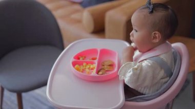 Küçük bir kız sabah sandalyesinde kahvaltı ederken elleriyle tabağından yemek yiyor..