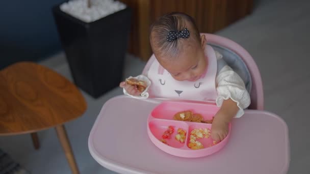 彼女の椅子に座ってシリコーンプレートから彼女の手で食べる赤ちゃん — ストック動画