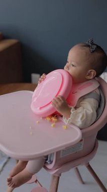 Elleri sandalyede oturan bir bebek yemek yiyor. Bebekler için tamamlayıcı beslenme
