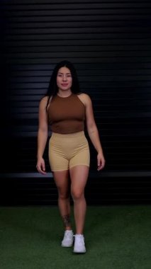 Sportif vücutlu genç bir kadın kameraya doğru yürür ve kollarını kavuşturur. Spor reklamcılığı konsepti
