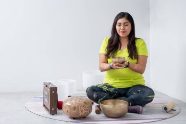 Meksikalı bir kadın elinde Tibet şarkı kasesi tutarken yoga stüdyosunda meditasyon yapıyor..