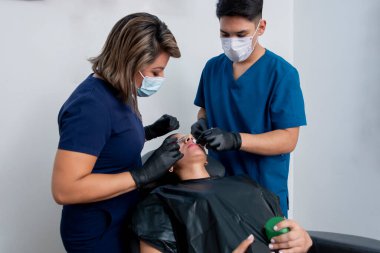Female doctor and her assistant applying botox to the lips of a young woman