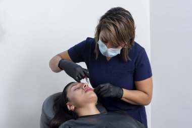 A doctor injecting botox into the lips of a young woman, in her beauticians office
