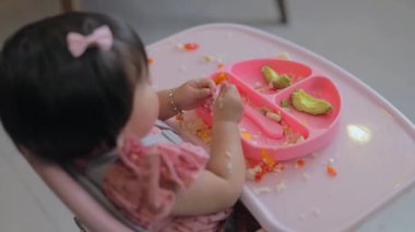 Küçük kız evde yemek yerken elleriyle tabağından yemek yiyor.