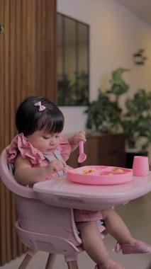 Kaşıkla yemek yiyen ve sandalyesinde oturan bir kızın ilk yemekleri.