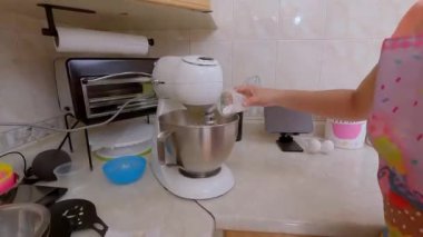 Kadın elektrikli miksere tuz ekliyor. Böylece unla karışıp bir parti hazırlıyor.