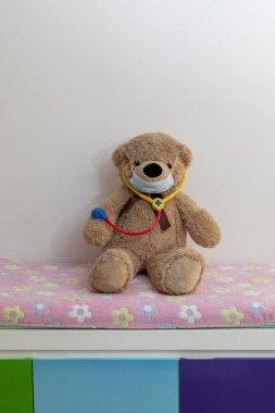 Pediyatri ofisinde sedyede duran steteskoplu oyuncak ayının yakın çekimi.