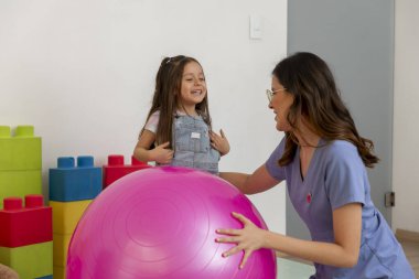 Çocuk doktoruyla seans sırasında spor topuyla oynarken gülen genç bir kız.