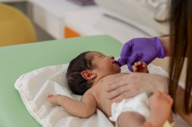 Mor eldivenli bir çocuk doktoru. Yeni doğmuş bir bebeği muayene ediyor. Doktorun muayenehanesinde yatıyor.