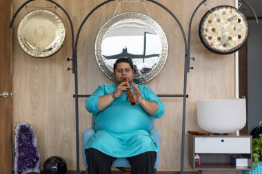 Meksikalı müzisyen, bir müzik stüdyosunda gonglar ve kristal kaseler arasında ses iyileştirme seansı sırasında Amerikan yerlisi flütü çalıyor.