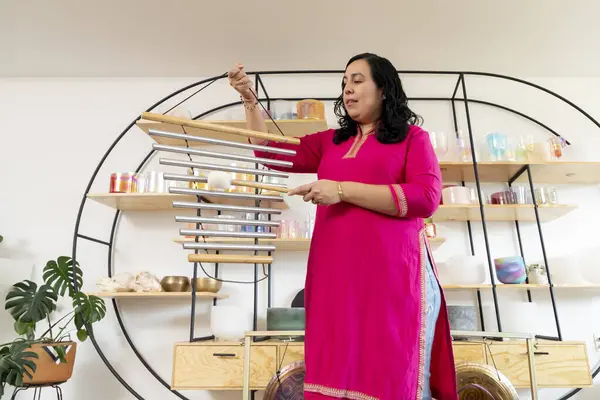 Bir müzik stüdyosunda rüzgar çanları çalan Latin bir kadın ses iyileştirme konusunda uzmanlaşmış, etrafında Tibet kâseleri, gonglar ve pervaneler var.