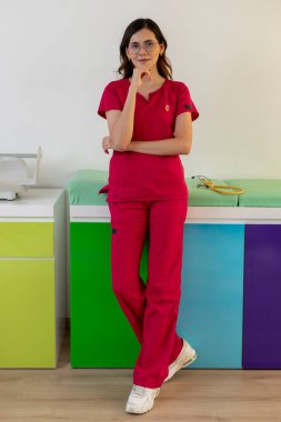 Kendine güvenen genç bir çocuk doktoru, enerjik ve modern ofisinde düşünceli bir şekilde poz veriyor.