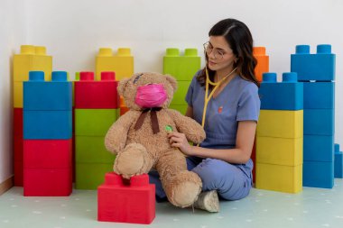 Klinikte ya da hastane oyun odasında oyuncak ayıya steteskop kullanan genç bir çocuk doktoru.