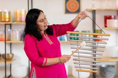 Bir müzik stüdyosunda müzik seansı için rüzgar çanları çalan Meksikalı kadın, müzik terapisi yoluyla rahatlama ve refahı teşvik ediyor.