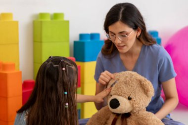 Latin bayan pediyatrist, Meksika 'daki parlak renkli ofisinde genç bir kıza tıbbi prosedürleri açıklamak için oyuncak ayıyı kullanıyor.