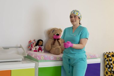 Canlı bir klinikte oyuncaklarla gülümseyen önlüklü çocuk hemşiresi.