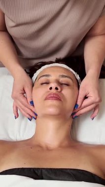 Profesyonel yüz masajı yapan yetenekli bir güzellik uzmanı. Rahatlamış bir müşteriye. Huzurlu bir sağlık merkezindeki tedavi masasında dinleniyor.