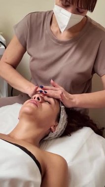Profesyonel güzellik uzmanı spa ya da güzellik salonundaki bir müşteriye rahatlatıcı yüz masajı yapıyor.