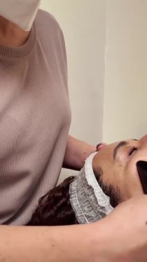 Profesyonel güzellik uzmanı masaj masasında yatan bir müşterinin yüzüne Gua sha taşıyla masaj yapıyor.