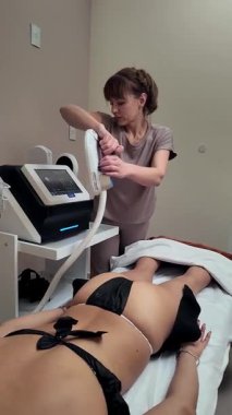 Profesyonel güzellik uzmanı vakum bardaklarıyla ilgileniyor, tedavi masasında dinlenen hastaya anti-selülit masaj tedavisi hazırlıyor.