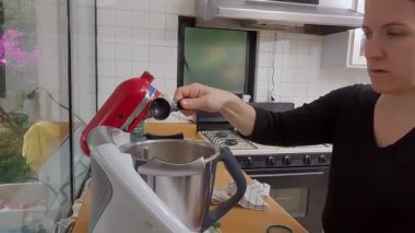 Kadın malzemeler ekliyor ve mutfakta kiş hamuru hazırlamak için karıştırıcı kullanıyor.