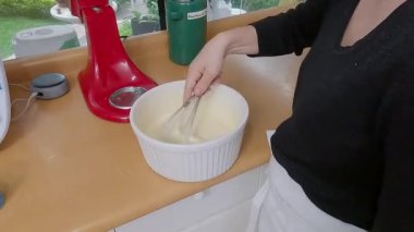 Yetenekli pasta şefi kiş için taze malzemeler çırpıyor, aromaları beyaz seramik kasede karıştırıyor, mutfak tezgahında.