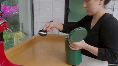 Profesyonel fırıncının iş yüzeyini un ile ilaçlaması, ticari mutfak çalışma alanındaki yeşil konteynırı kavraması