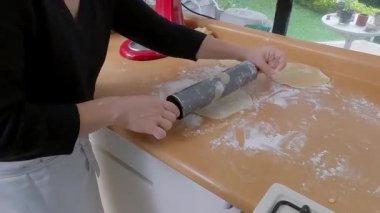 Kadın un yüzeyde yuvarlanan hamur daireler, parlak mutfak çalışma alanında ahşap oklu ev yapımı kiş hazırlıyor