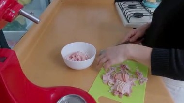 Profesyonel şef, jambonu canlı yeşil kesme tahtasıyla dikkatlice küçük parçalara ayırarak yaklaşan aşçılık yaratımı için gerekli malzemeleri hazırlıyor.