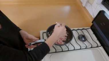 Profesyonel ev aşçısı gaz sobası yanında çıtır çıtır domuz pastırması doğruyor, tava cızırdıyor mutfağı parlak, temiz çalışma alanını yansıtıyor ve özenle malzemeleri hazırlıyor.