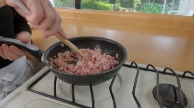 Profesyonel aşçı pastırma dilimliyor, tavada et pişiriyor ve modern mutfak çalışma alanında ahşap çatalla kiş pişiriyor.