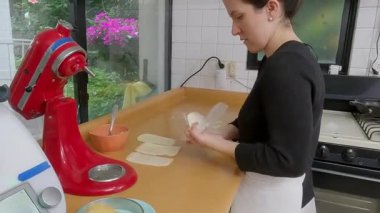 Profesyonel bir fırıncı hamur karelerine tereyağı sürüyor. Parlak bir mutfakta kiş için malzemeler hazırlıyor.