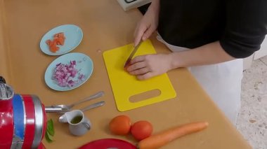 Şef sarı bir kesme tahtasında havuç doğruyor, ev mutfağında lezzetli bir yemek için malzemeler hazırlıyor.