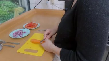 Ev yemeği dikkatlice soyuluyor parlak turuncu havuç sarı kesme tahtasında, eller düzenli olarak çalışırken yaklaşan yemek için taze malzemeler hazırlıyor.