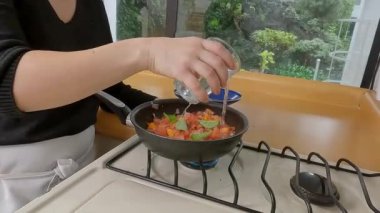 Profesyonel aşçı ev yapımı domates sosu hazırlıyor, dikkatlice su ve otlar ekliyor, tavayı kaplarken mutfakta gaz sobasında kaynıyor.