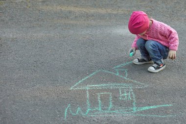 Küçük kız tebeşirle bir ev çiziyor.