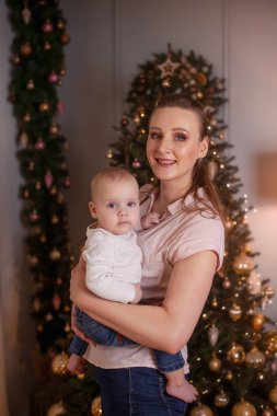 Anne kucağında bir Noel ağacının arka planında bebeği tutuyor. Yılbaşı fotoğrafı.