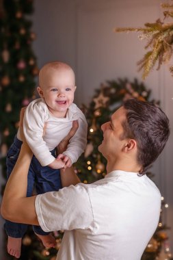 Babam bebeği bir Noel ağacının arka planına doğru kaldırıyor. Noel 'in Mutluluğu