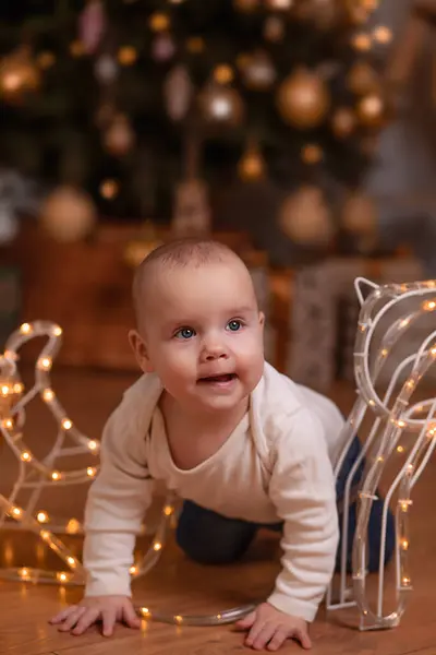 Bir bebek odanın içinde bir Noel ağacının arka planına doğru sürünüyor. Tatilin atmosferi, yeni yılın havası. Bir çocuğun hayatındaki ilk Noel. Ev ortamı