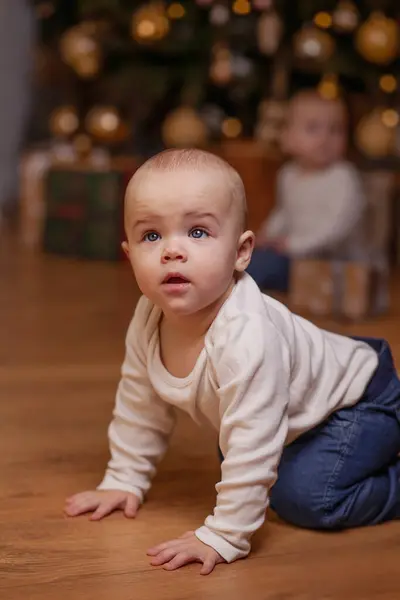 Bir bebek odanın içinde bir Noel ağacının arka planına doğru sürünüyor. Tatilin atmosferi, yeni yılın havası. Bir çocuğun hayatındaki ilk Noel. Ev ortamı