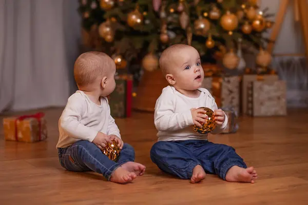 İkiz çocuklar evin Noel ağacının yanında yerde oturuyorlar. Yeni yıl havası.