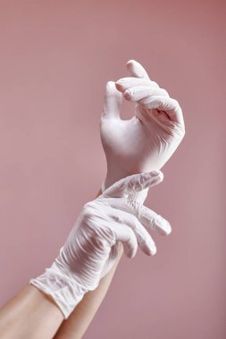 Pembe arka planda beyaz tıbbi eldivenli eller. İş için hazırlanılıyor