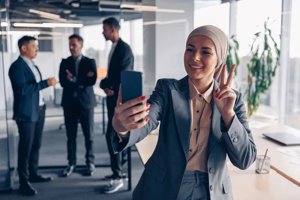 Muslim business woman in hijab taking selfie on colleagues background in office. High quality photo
