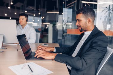 Afrikalı iş adamı modern ofiste otururken dizüstü bilgisayarda çalışıyor. Yüksek kalite fotoğraf